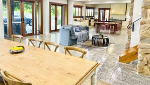 A spacious living area with a wooden dining table, a grey sofa, and a kitchen in the background.