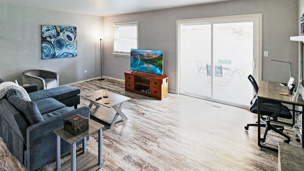 A living room with a sofa, coffee table, TV on a wooden stand, and a sliding glass door leading to a balcony. - Remodeled Broken Arrow Home -Dogs OK -Safe Location -Fully Privacy Fenced Yard  (Broken Arrow)