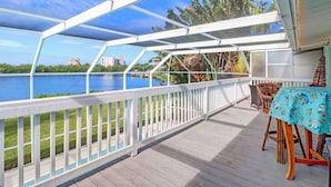A covered outdoor deck with a view of a lake and buildings in the distance. - Bayfront Duplex! Gulf Access w/ Dock, Pool, Bikes, Kayak & Over $100 of Free Daily Activities! (Bonita Springs)