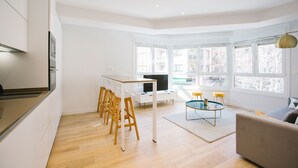 A modern living room with a dining area, large windows, and a kitchen. - E 2 BEDROOM FAMILY APARTMENT SAN MARCIAL 33 (San Sebastián)