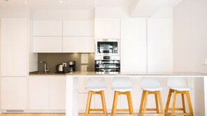 A modern kitchen with white cabinetry, a stainless steel oven, and a bar area with four stools. - E 2 BEDROOM FAMILY APARTMENT SAN MARCIAL 33 (San Sebastián)