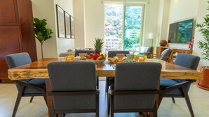 A dining area with a wooden table, grey upholstered chairs, and a fruit bowl with oranges and pineapple. - New renovated Penthouse in V399! 2BD Penthouse for rent in Old Town, Puerto vall (Puerto Vallarta)
