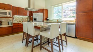 A modern kitchen with wooden cabinets, a granite countertop, and a built-in island with bar stools. - New renovated Penthouse in V399! 2BD Penthouse for rent in Old Town, Puerto vall (Puerto Vallarta)