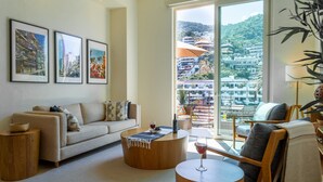 A modern living room with a sofa, coffee table, and chair, a large window with a view of buildings, and framed pictures on the wall. - New renovated Penthouse in V399! 2BD Penthouse for rent in Old Town, Puerto vall (Puerto Vallarta)
