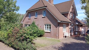 A large brick house with a steeply pitched roof, a chimney, and a well-maintained garden with a bench. - Haferweg 2, Strandnelke EG - Haferweg 2, Strandnelke (Wyk auf Föhr)