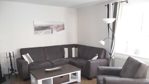 A modern living room with a sectional sofa, a coffee table, and a floor lamp. - Haferweg 2, Strandnelke EG - Haferweg 2, Strandnelke (Wyk auf Föhr)