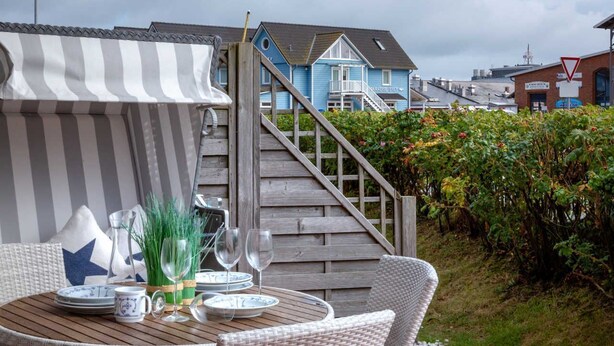 A wooden deck with a table set for dining, surrounded by wicker chairs. A striped awning provides shade. - Beach time, Germany (List)