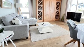 A modern living room with a grey sofa, a white coffee table, a wooden cabinet, and a TV. - Beach time, Germany (List)