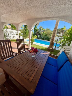 A wooden table with a vase of flowers, blue cushioned seating, and a view of a swimming pool.