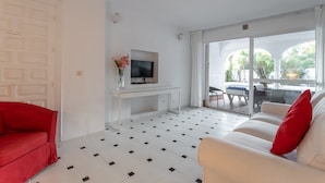 Sala de estar com televisão, sofá vermelho, sofá branco e uma grande porta de vidro deslizante que dá para uma área externa.