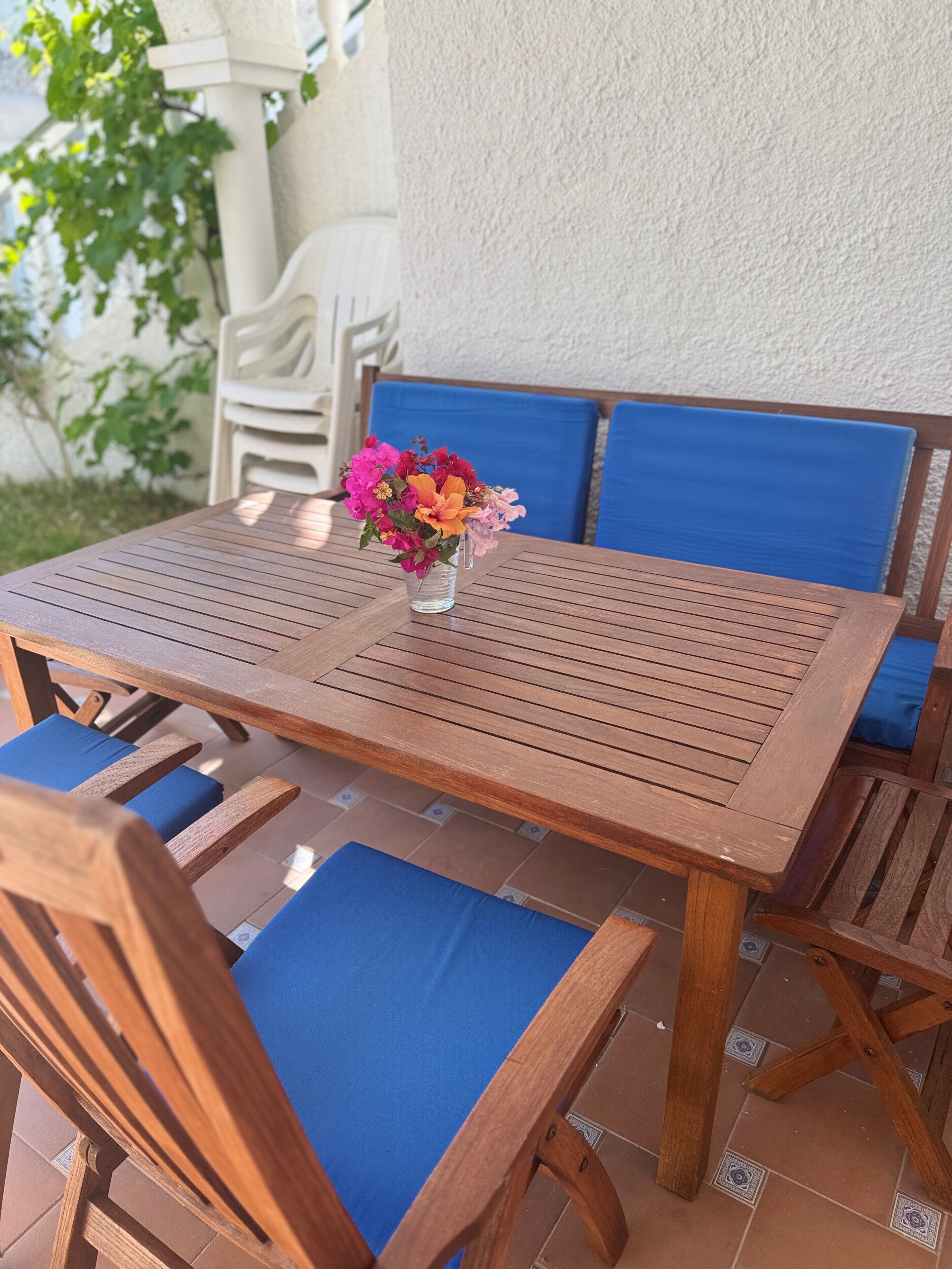 Un tavolo di legno con sedie imbottite blu, un vaso di fiori e una parete bianca sullo sfondo.