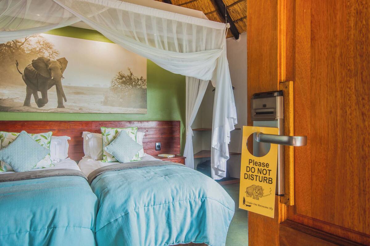 A bedroom with two beds, a mural of an elephant, and a 'Please do not disturb' sign.