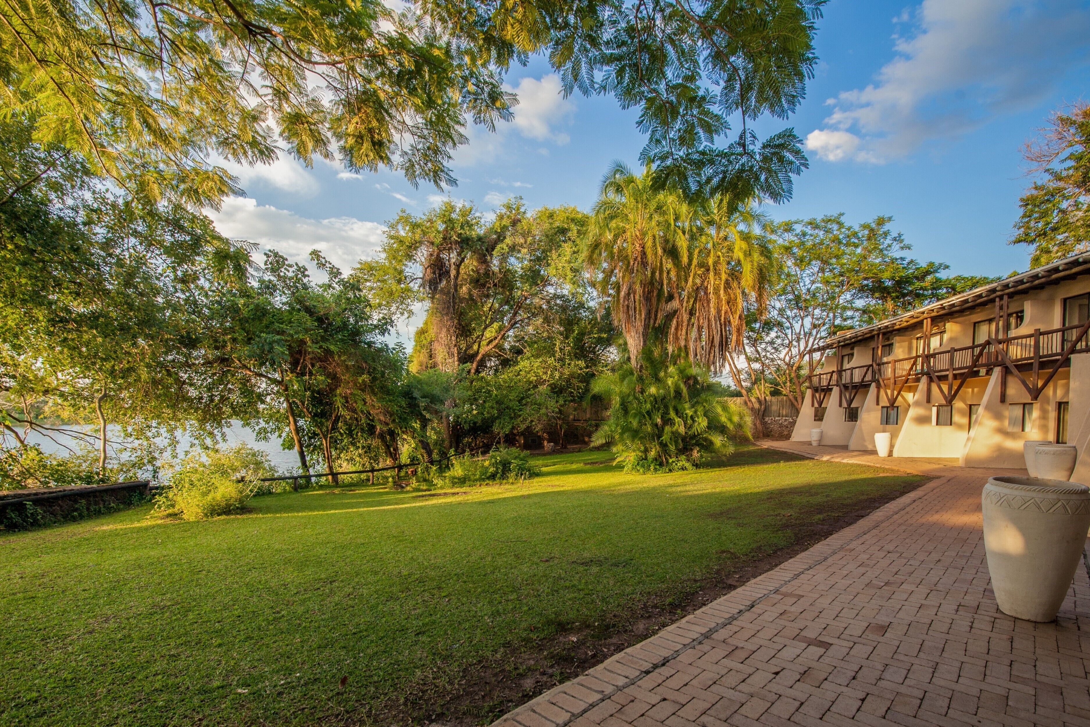 A courtyard with a brick pathway, lush greenery, and a building with a traditional architectural style.