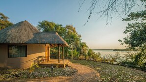 A thatched-roof building with a patio and a view of a lake. - Chobe Safari Lodge (Kasane)