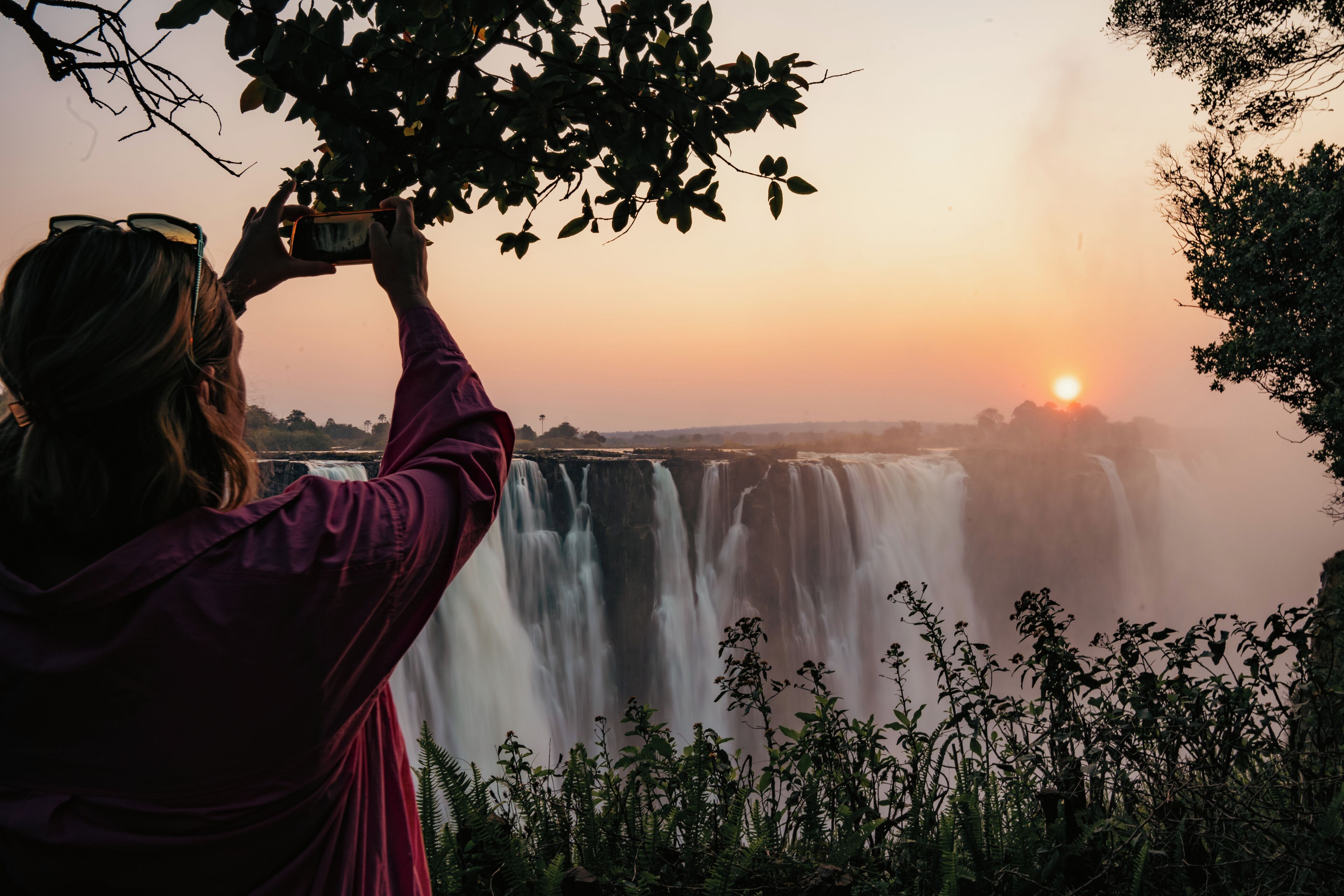 A person taking a photo of a waterfall at sunset.
