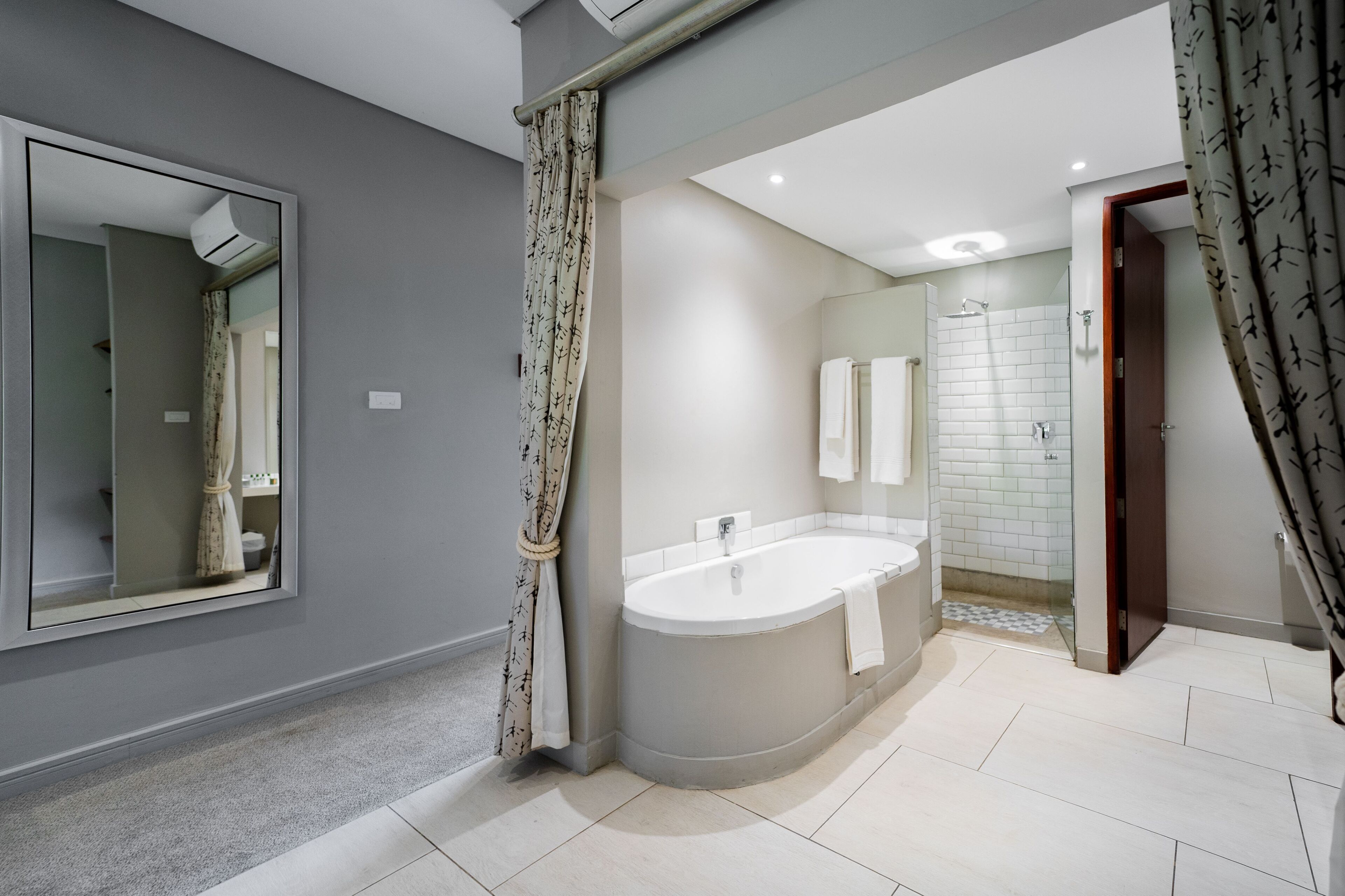 A modern bathroom with a large bathtub, a shower, and a mirror.