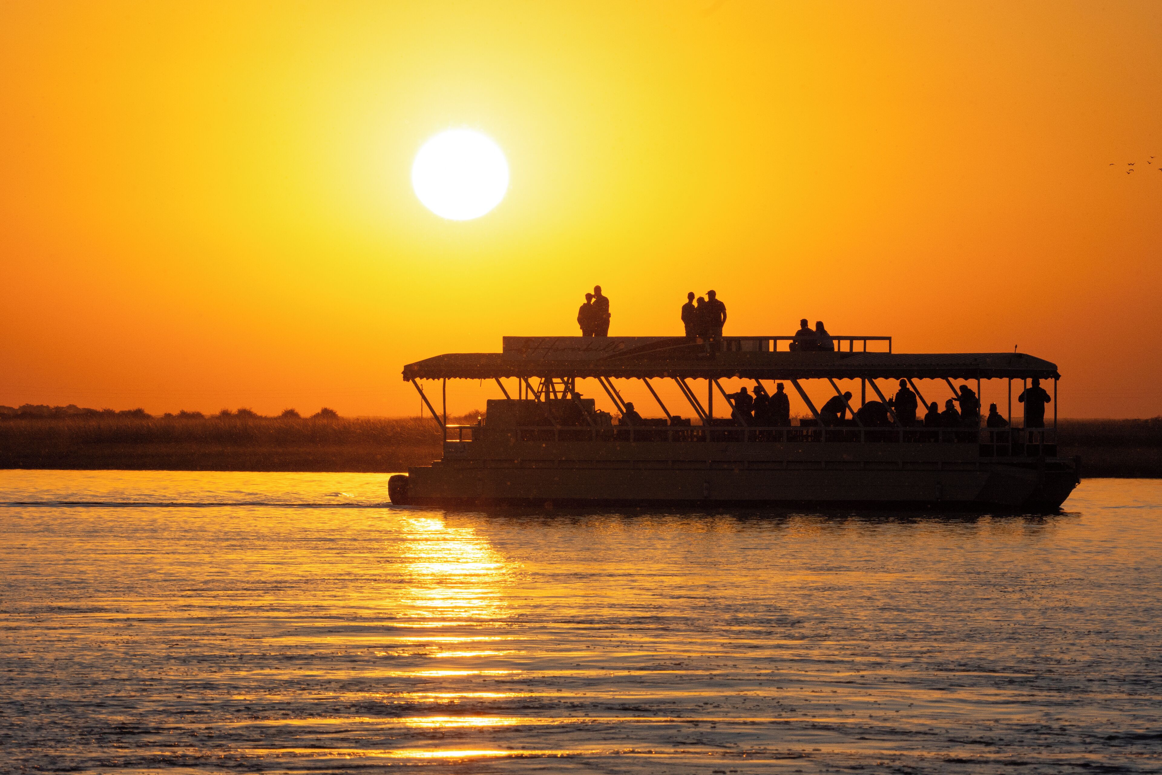 A boat with passengers silhouetted against a sunset.