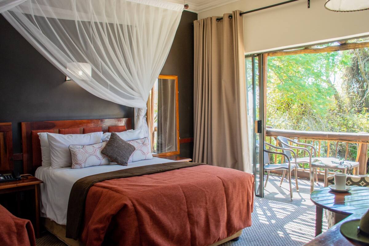 A bedroom with a bed, a nightstand, a bedside table, a window with curtains, and a balcony with outdoor furniture.