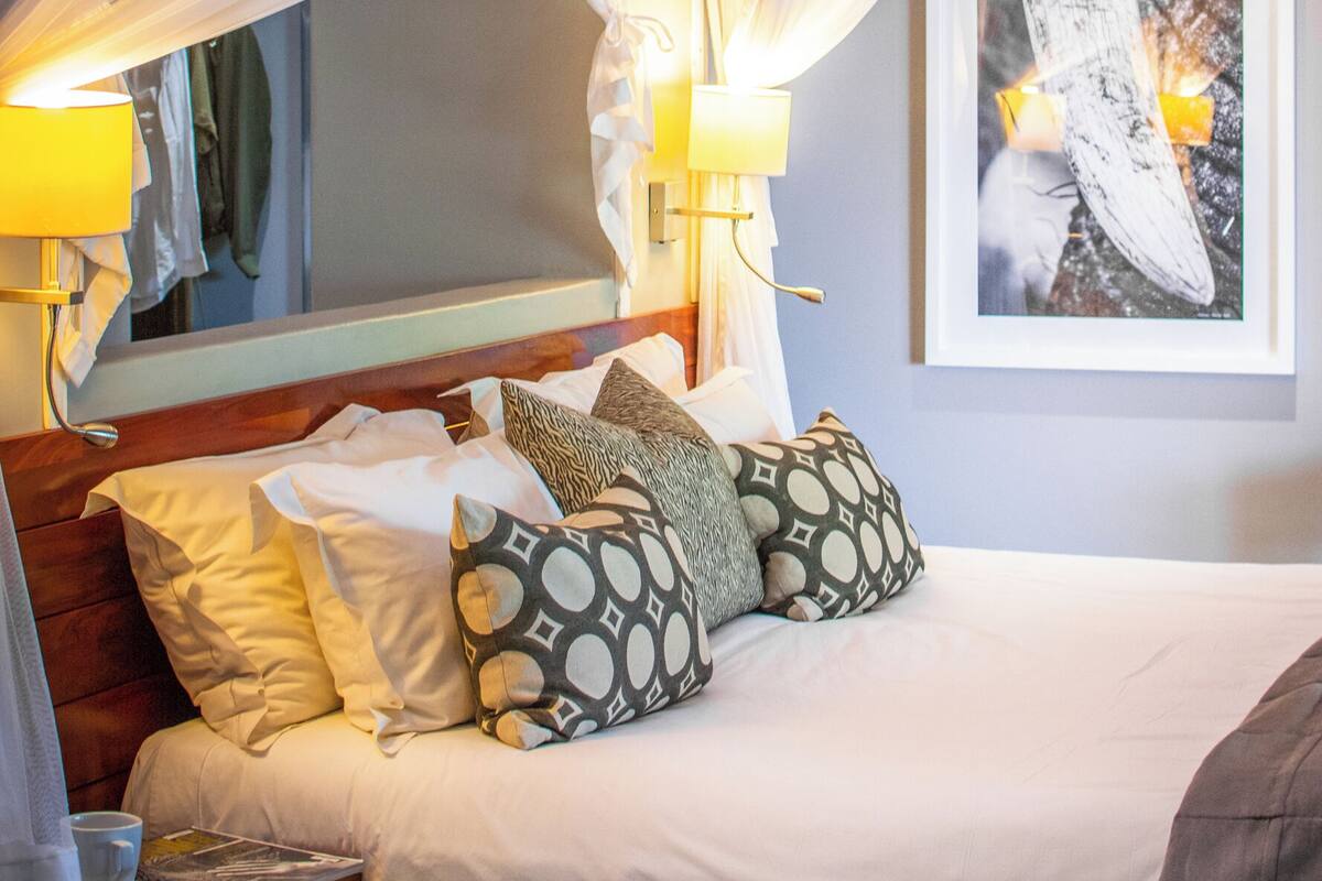 A bedroom with a canopy bed, bedside lamps, a framed picture on the wall, and a bedside table with a cup and magazine.