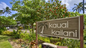 A sign for 'kauai kailani' with a palm tree logo, surrounded by lush greenery and a well-maintained garden.