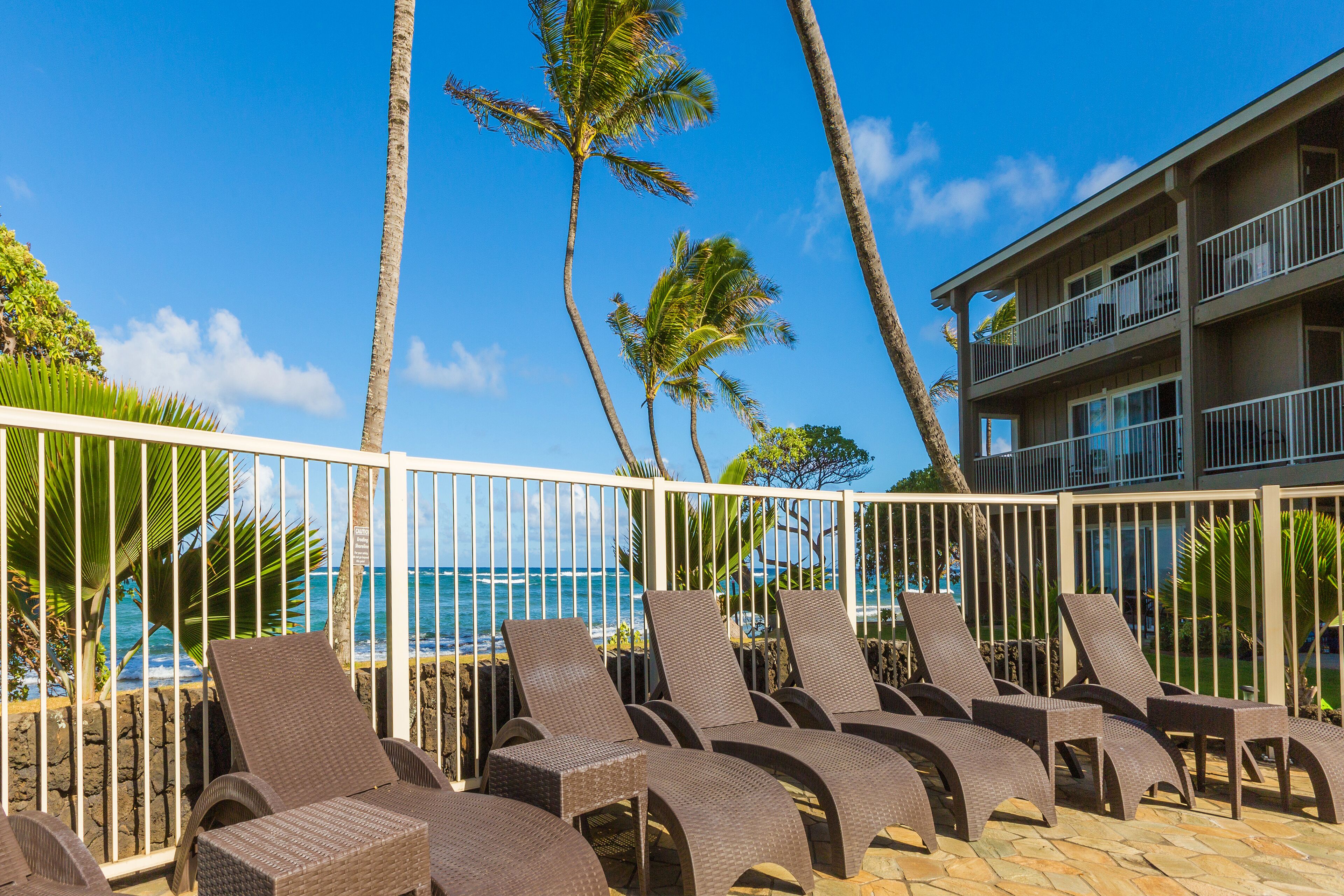 A poolside area with lounge chairs and a view of the ocean.