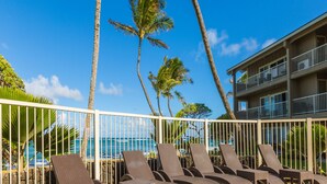 A poolside area with lounge chairs and a view of the ocean.