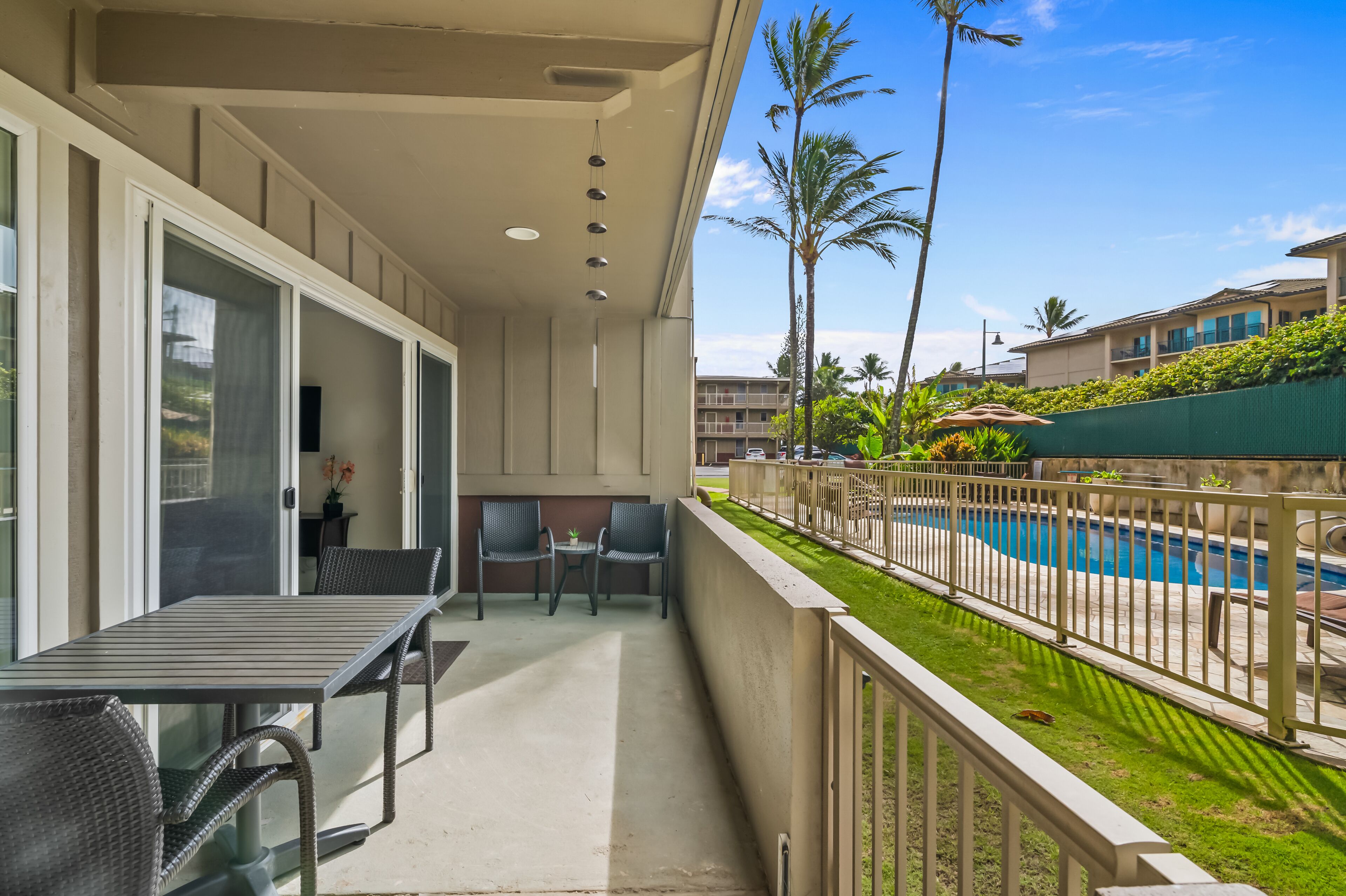 A balcony with a table and chairs, overlooking a swimming pool and palm trees.