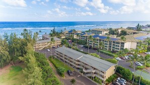 A coastal hotel with multiple buildings, a parking lot, and a view of the ocean.