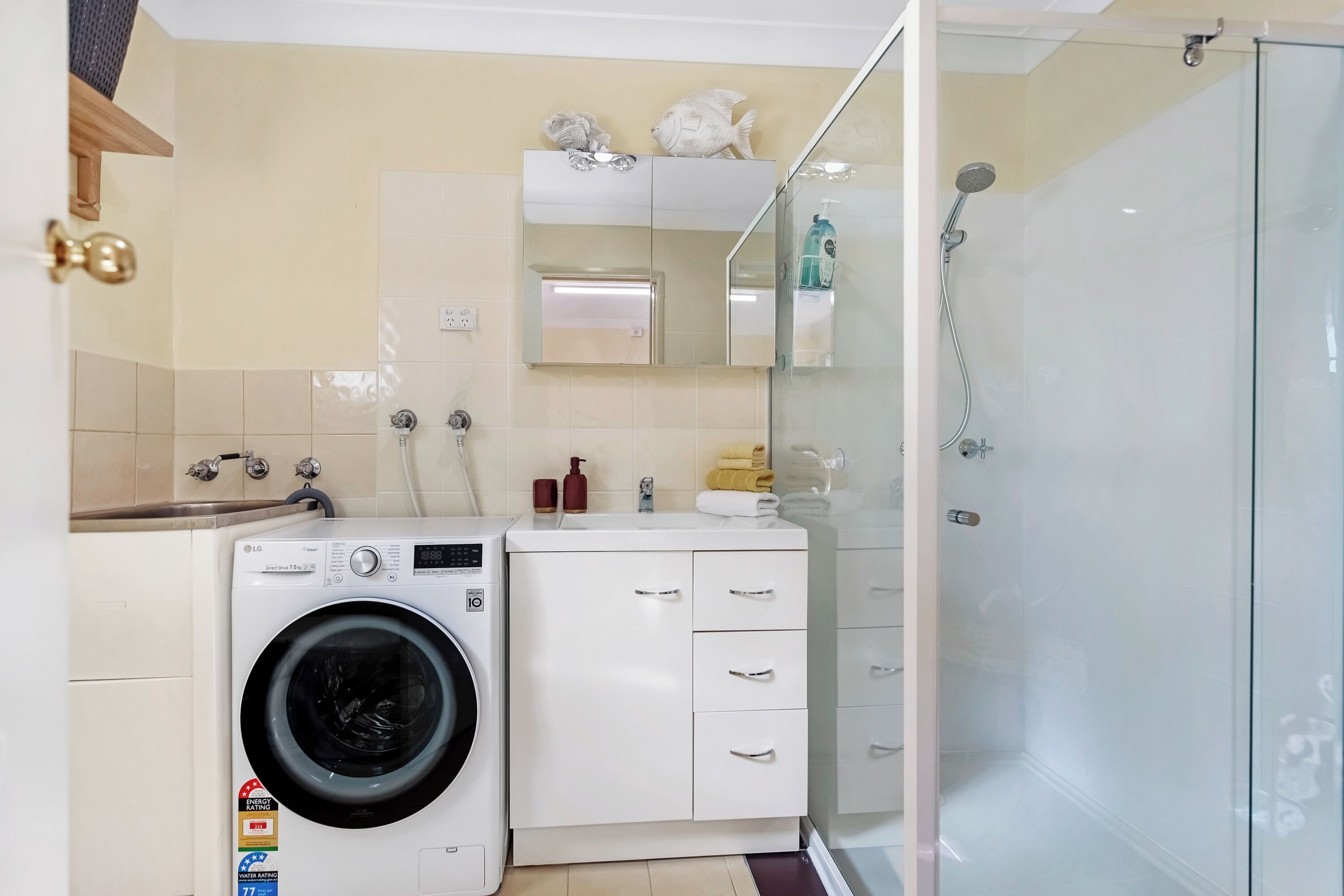 Een kleine badkamer met een wasmachine, een glazen douchecabine en een spiegel boven de wastafel.
