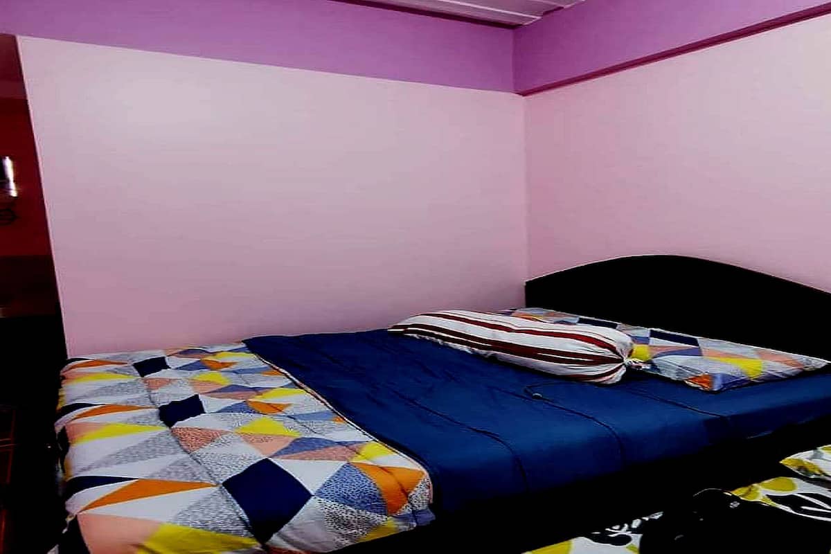 A single bed with a colorful quilt, a blue mattress cover, and striped pillows.