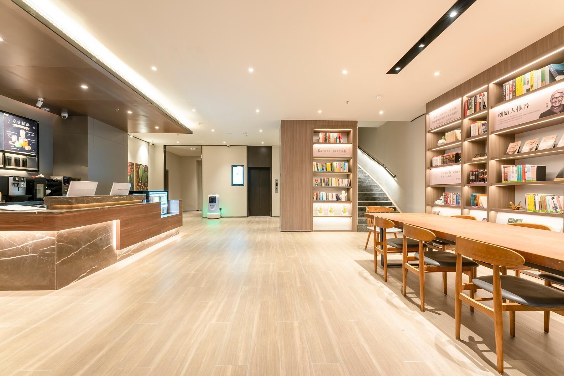 A modern hotel lobby with a reception desk, a staircase, and a bookshelf filled with books.