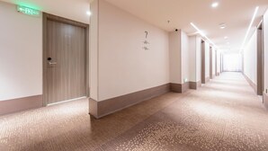 Pasillo de hotel con piso alfombrado, puertas de madera y un letrero de salida verde.
