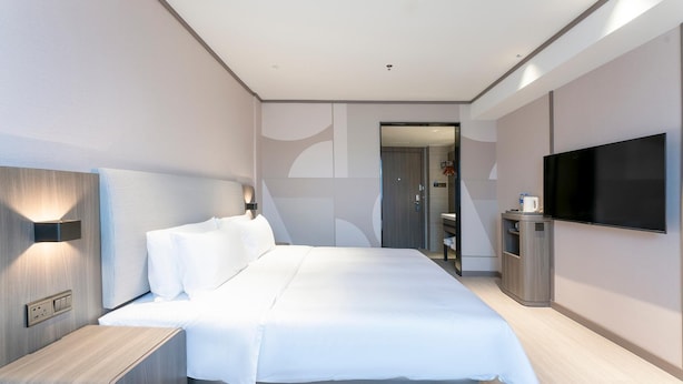Una habitación de hotel moderna con una cama grande, un televisor, una mesita de noche y un armario.