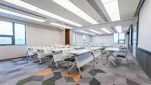 Un salón de conferencias con varias mesas, sillas y una pantalla para proyector.