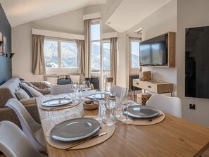 A modern dining area with a wooden table set for four, a sofa, and a TV mounted on the wall.