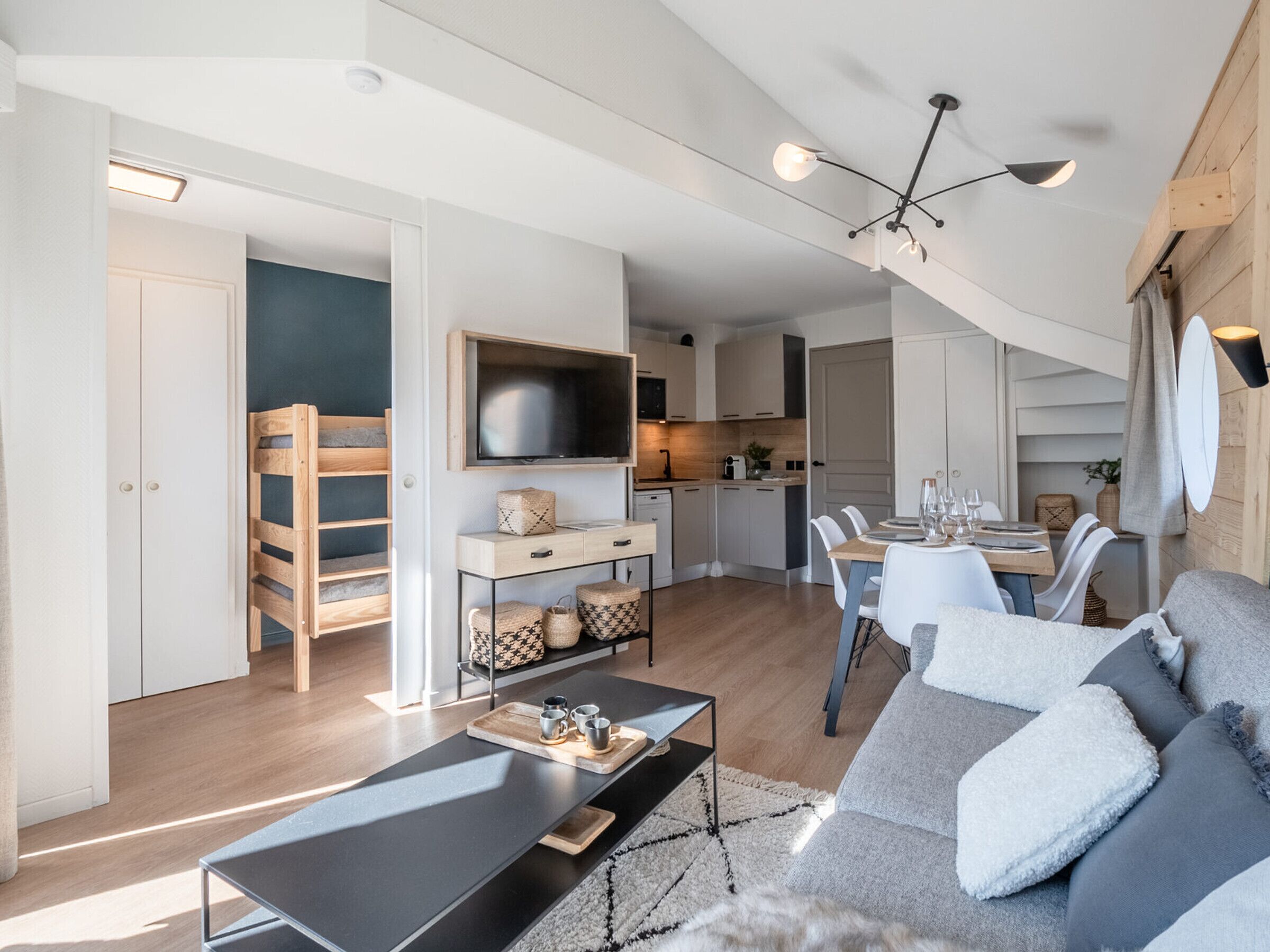 A modern apartment with a living room, dining area, kitchen, and a staircase.