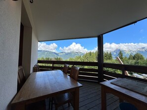 A wooden deck with a table and chairs, overlooking a mountainous landscape with trees and a clear sky.