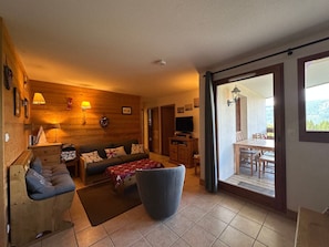 A cozy living room with a wooden wall, a sofa, a television, and a dining area with a table and chairs.