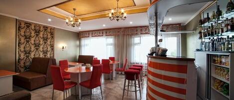 A hotel lobby with a bar area, red chairs, a sofa, and a patterned wall.