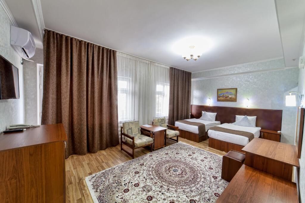 A hotel room with two beds, a desk, a chair, a rug, and a painting on the wall.