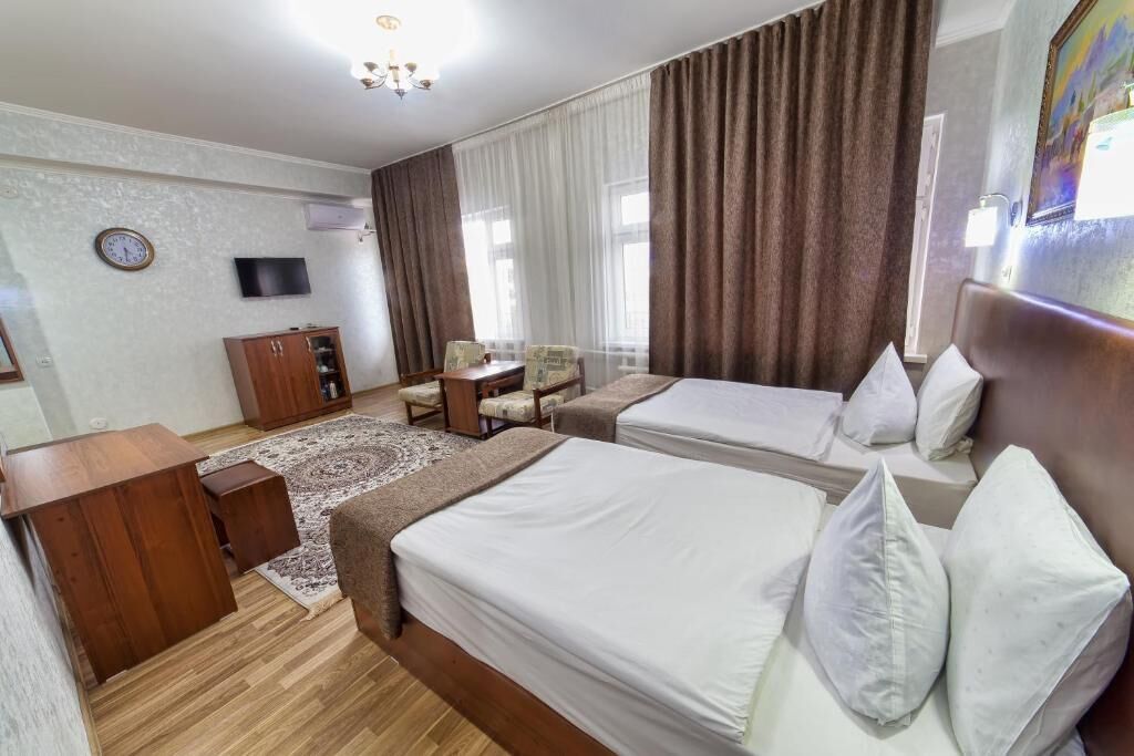 Ein Hotelzimmer mit zwei Betten, einem Schreibtisch, einem Stuhl, einem Fernseher und einem großen Fenster mit Vorhängen.