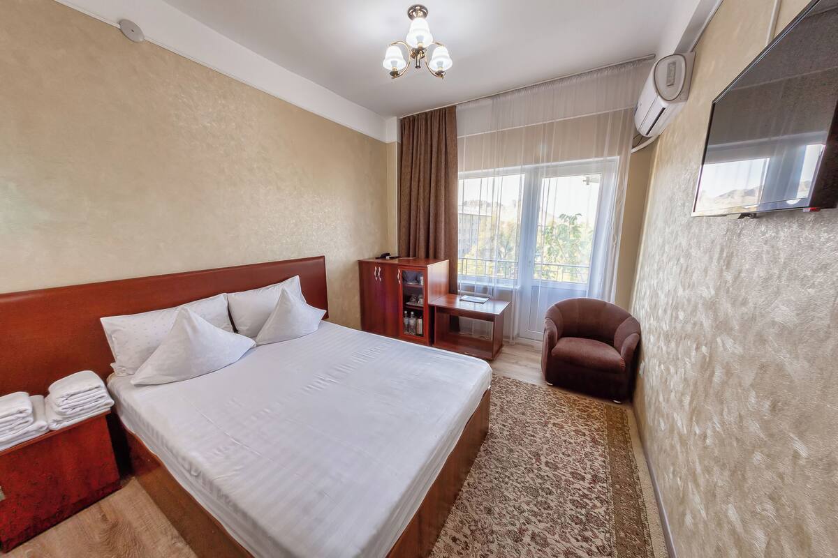 A hotel room with a bed, a desk, a chair, a TV, and a window with curtains.