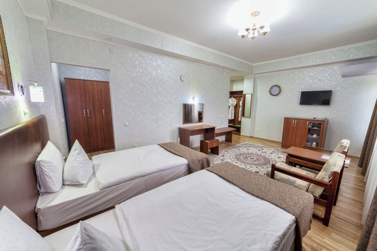 A hotel room with two single beds, a desk, a chair, a wardrobe, a television, and a clock on the wall.