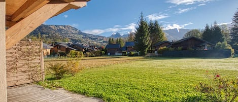 A wooden deck leading to a grassy area with houses in the background and mountains in the distance.