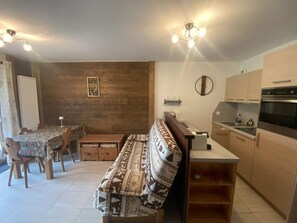 A compact kitchen with modern appliances, a dining area with a wooden table and chairs, and a bench with a patterned cushion.