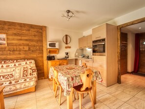 A cozy kitchen with wooden cabinets, a dining table with chairs, a microwave, and a coffee maker. - Charming T3 with terrace and mountain view, 2 bedrooms in Morillon (Morillon Village)
