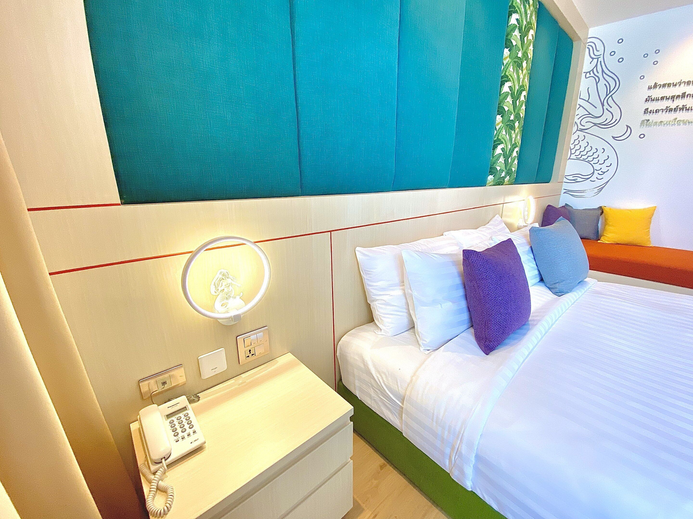 A hotel room with a bed, bedside table with a phone, and a wall-mounted light.