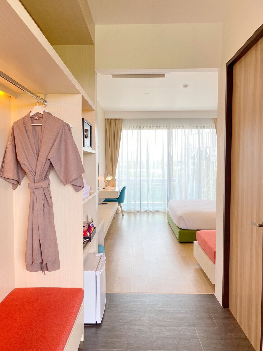 Habitación de hotel con cama, escritorio, silla, bata colgando y un banco.