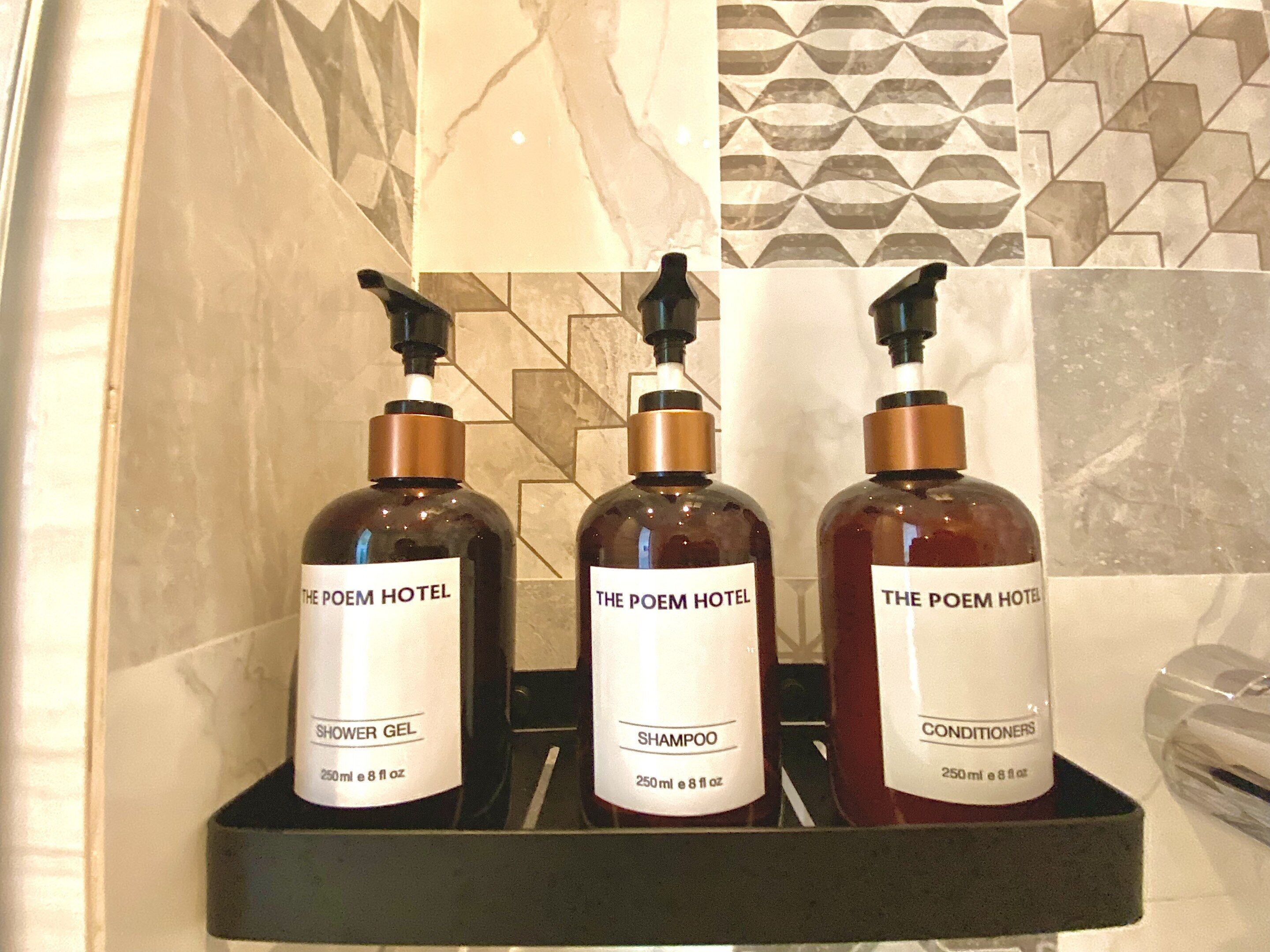 Tres botellas de artículos de tocador de hotel: gel de ducha, champú y acondicionador, sobre una estantería.