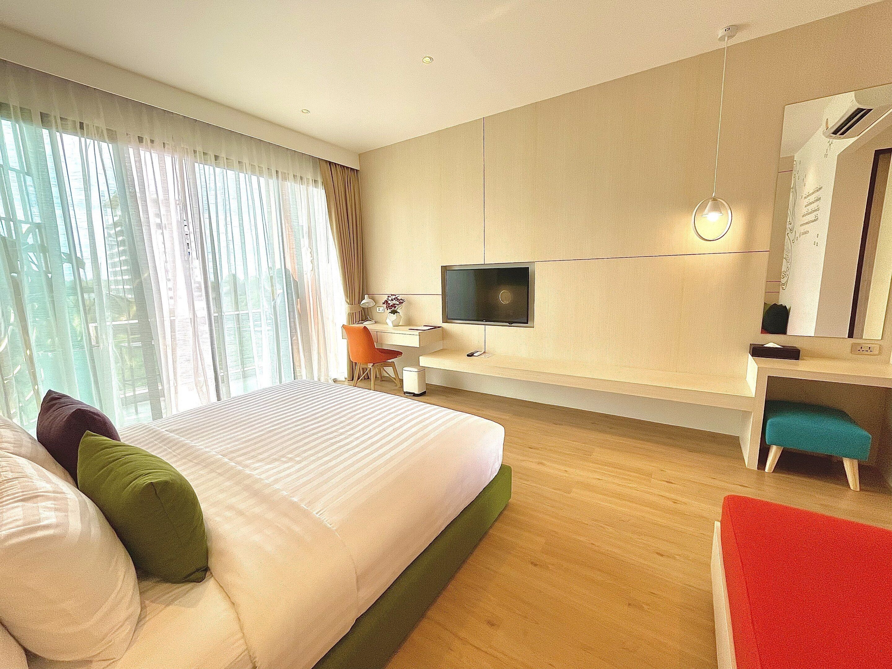 A modern hotel room with a large bed, a desk with a computer, a TV, and a mirror.